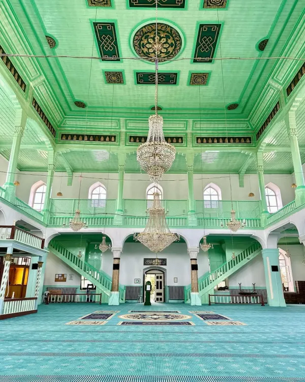 Geniş bir caminin iç mekanında yeşil tonlarında süslemeler ve avize.