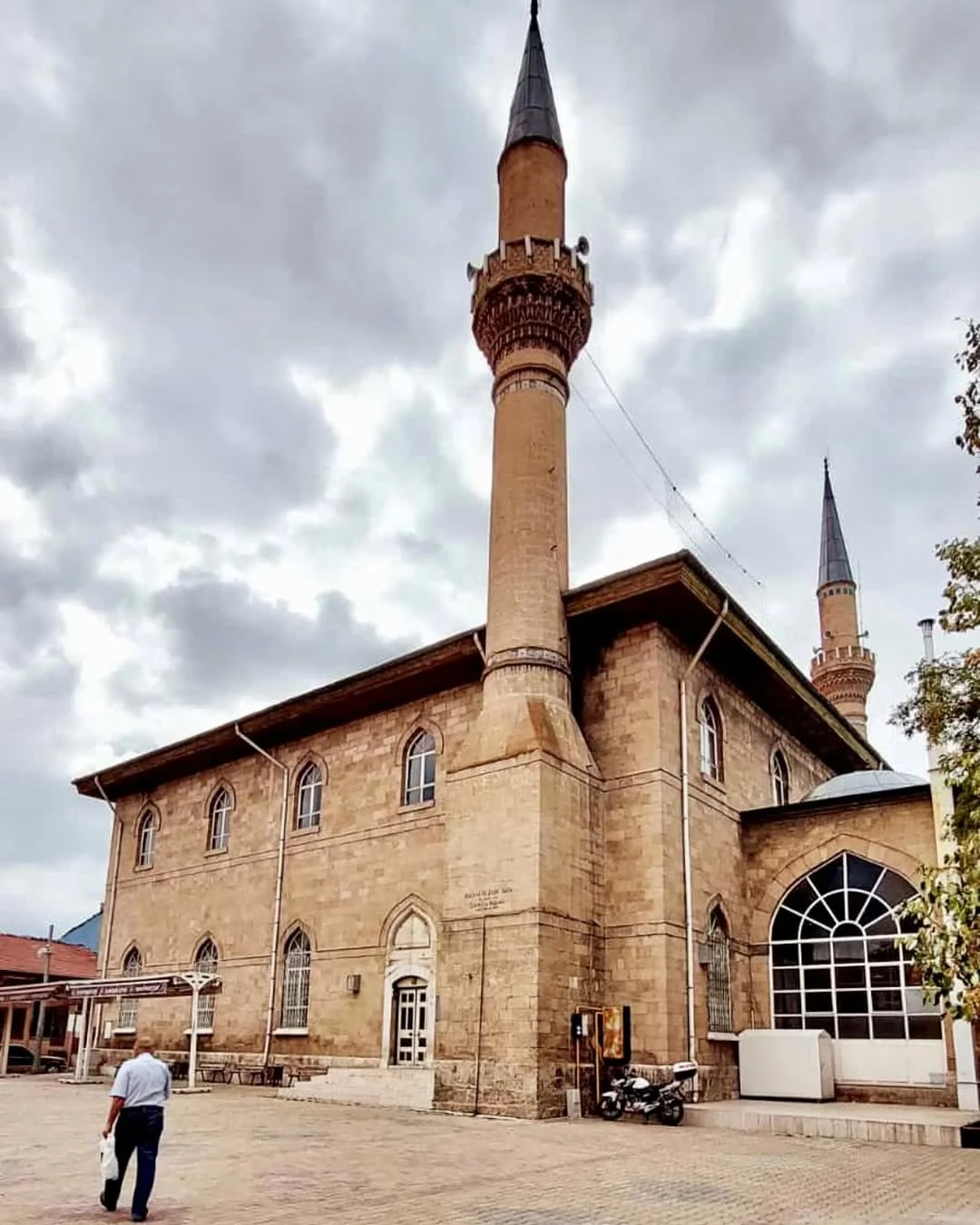Tarihi Ulu Cami yapısı ve yanında yüksek minare, arka planda bulutlu gökyüzüyle dikkat çekiyor.