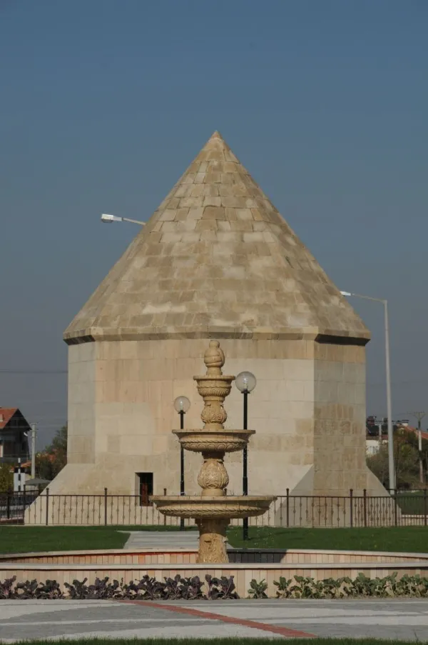 Kesik koni şeklinde taş yapı, zarif üç katlı çeşme ve yeşil alan.