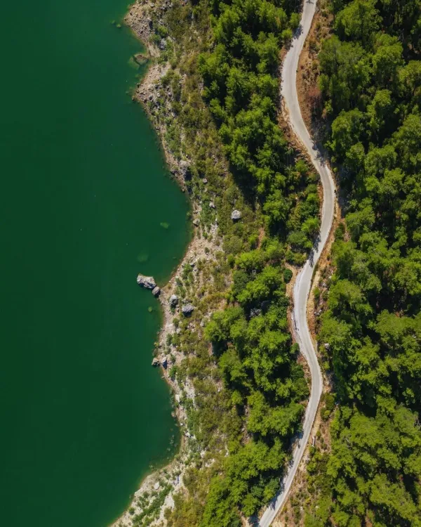 Yemyeşil ormanlarla çevrili, derin yeşil su ve kıvrımlı yol manzarası.