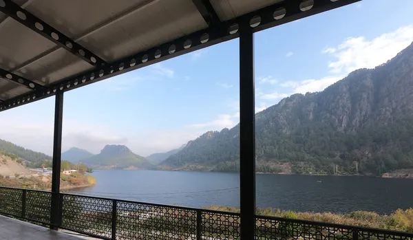 Göl manzarası, dağlar ve yeşil ağaçlarla çevrili bir terastan görüntü.