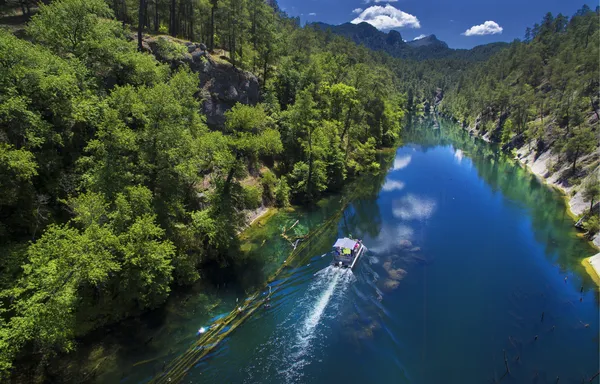 Yemyeşil ağaçlarla çevrili Karacaören Barajı'nın derin mavi suyu ve tekne.