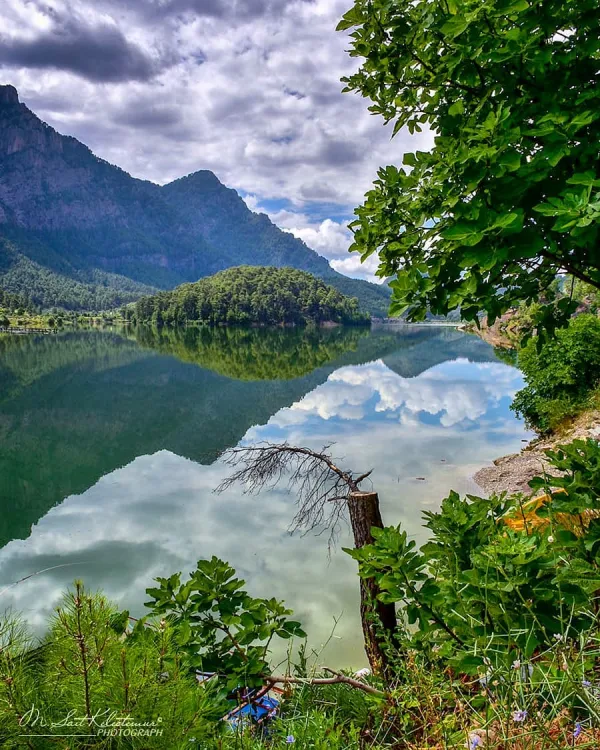Dağlarla çevrili Karacaören Barajı göl manzarası, ağaç yansımalarıyla dolu