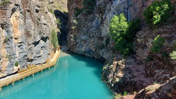 Dik kayalıklarla çevrili turkuaz su ve ahşap yürüyüş yolu