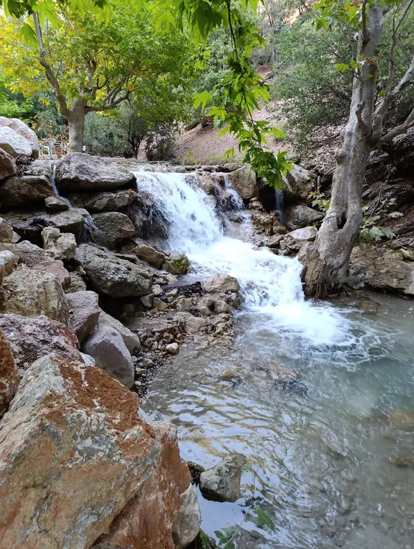 Karanlıkdere Kanyonu'nda kayaların arasından akan berrak bir şelale ve çevresindeki yeşil doğa.