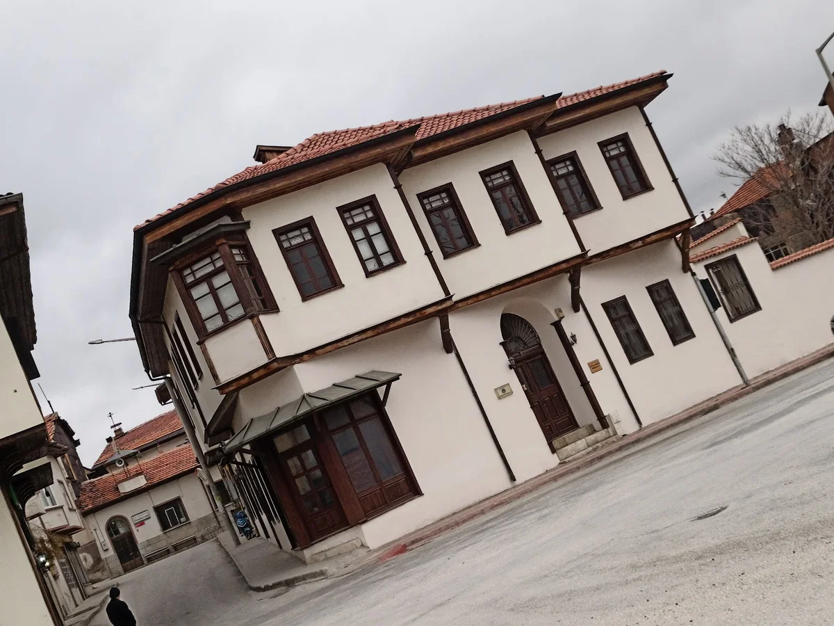 Geleneksel Mısırlılar Evi Mimarisinin Güzelliği: Burdur'da Tarihin İzleri! Geleneksel mimari tarzda iki katlı beyaz bina, ahşap çerçeveli pencereler ve kırmızı kiremitli çatı ile.