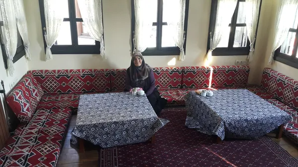 Kırmızı ve beyaz desenli döşemelerle kaplı oturma alanı, mavi masalar ve çay fincanları ile sıcak bir atmosfer sunuyor.