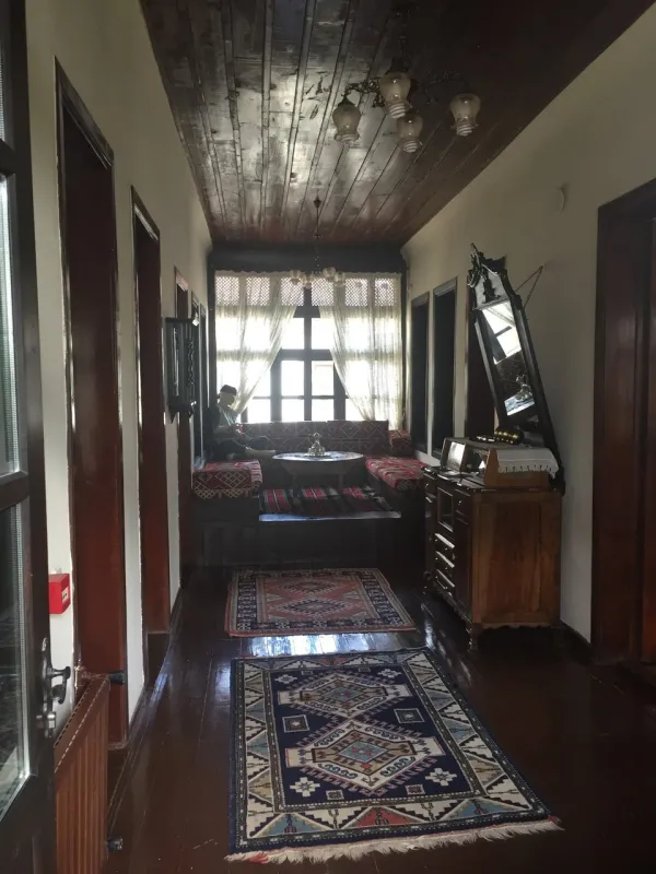 Uzun koridor ve ahşap tavanlı iç mekân, renkli yastıklı kanepe ve doğal ışık alan pencerelerle aydınlatılmış.