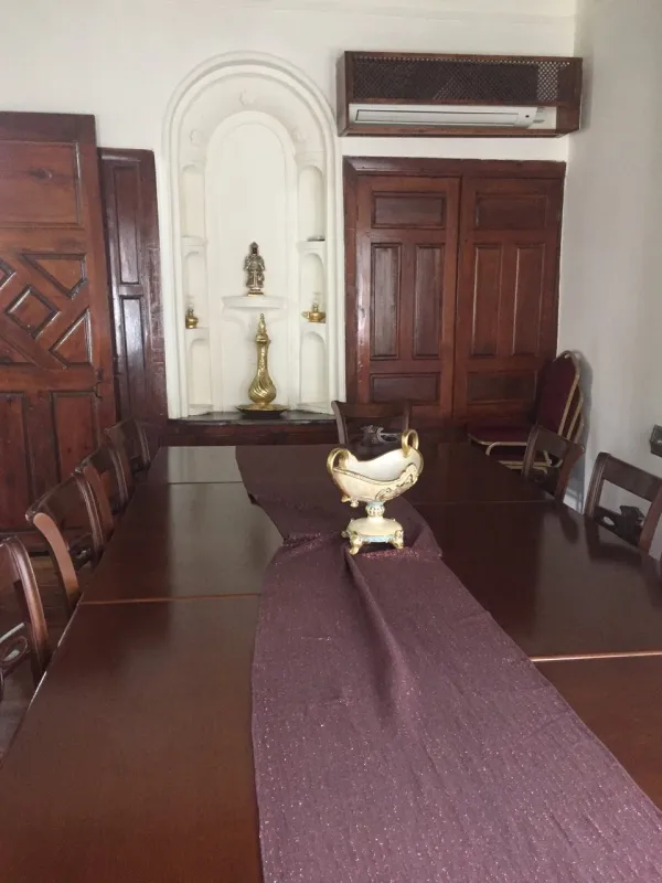 Klasik iç mekanda büyük ahşap masa, mor örtü ve süslü kase var.