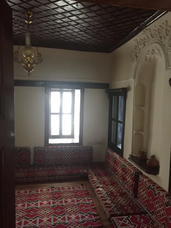 Açık tonlarda duvarlarla aydınlatılan geleneksel oturma alanı, kırmızı desenli yastıklar ve avize ile sıcak bir atm