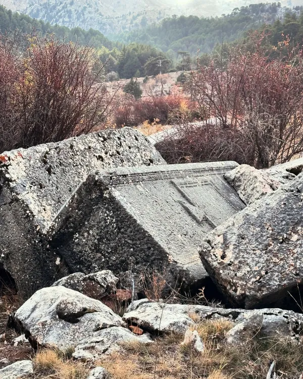Büyük taş bloklar, yosun kaplı kayalar ve dağlar arasında huzurlu bir doğa manzarası.