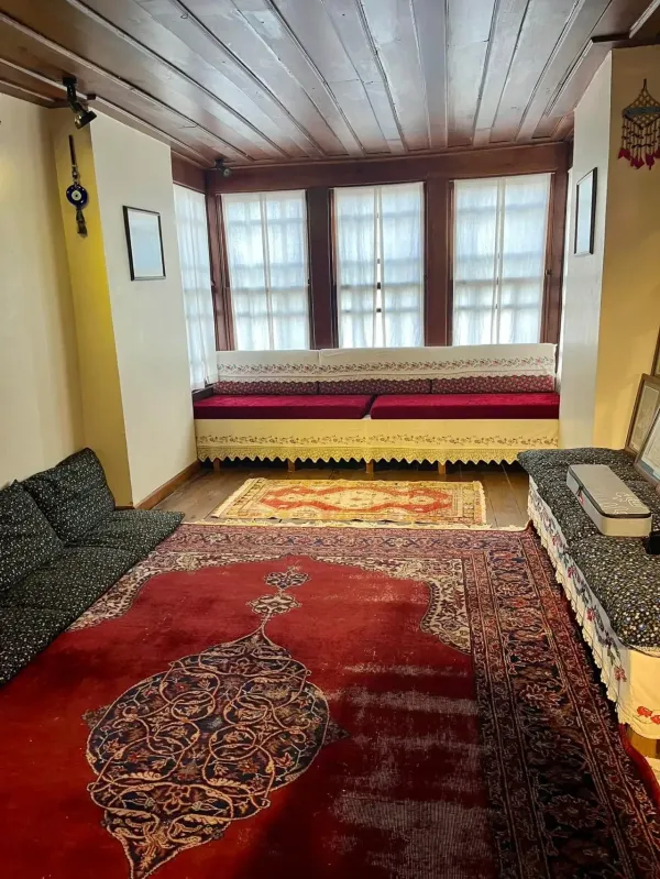 Geleneksel bir iç mekan, desenli halı ve oturma alanlarıyla sıcak bir atmosfer sunuyor.