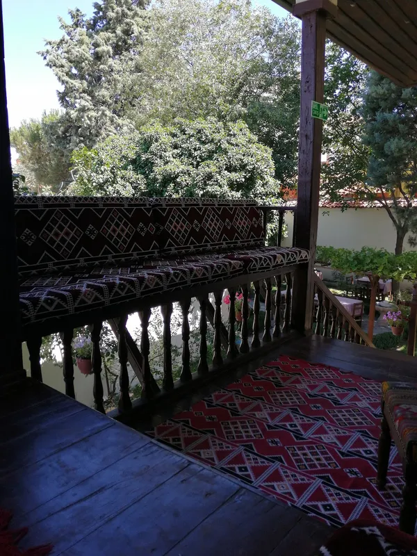 Ahşap terasta geleneksel motiflerle kaplı oturma yeri ve yeşil bitkiler