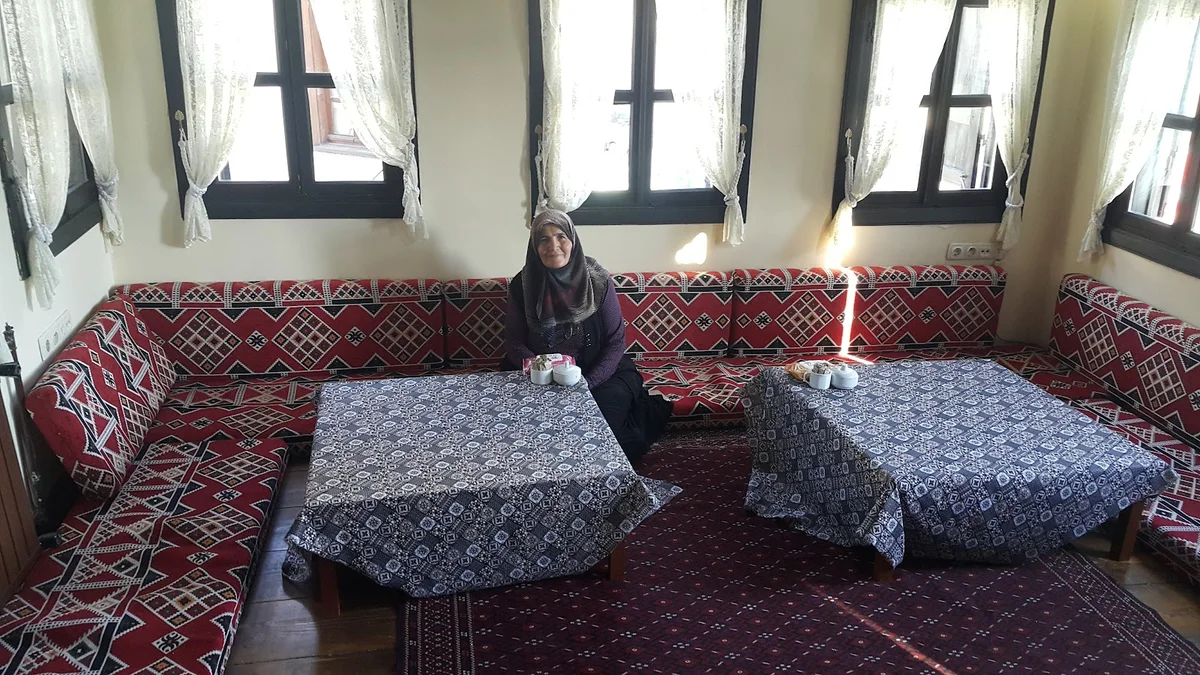 Geleneksel İç Mekan - Desenli Kanepe ve Çay Bardakları! Geleneksel iç mekan, desenli kanepe, çay bardakları ve geleneksel kıyafetli kadın ile samimi bir atmosfer.