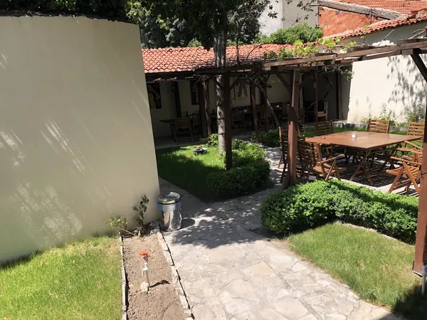 Yeşil bahçede taş döşeli yol, ahşap oturma alanı ve kırmızı çatılı bina