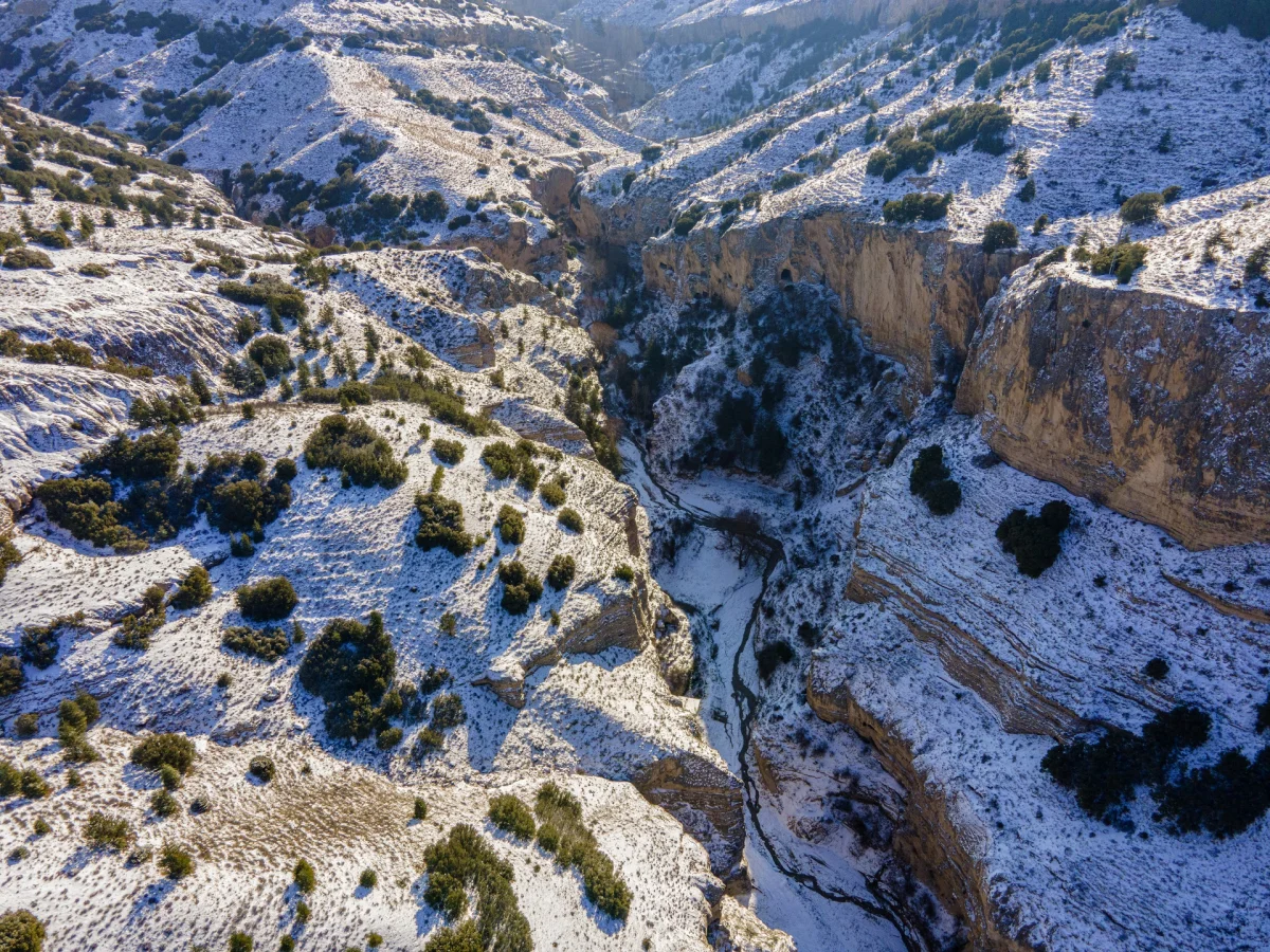Karla kaplı dağlar ve derin kanyon, ortasında akarsu ile doğal manzara.