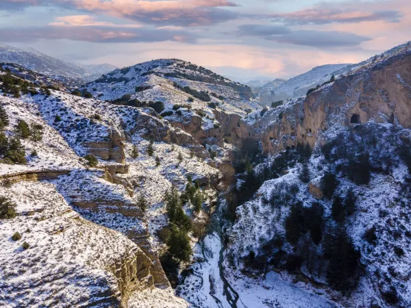 Karla kaplı dağlar, yeşil ağaçlar ve pastel tonlarda gün doğumu manzarası