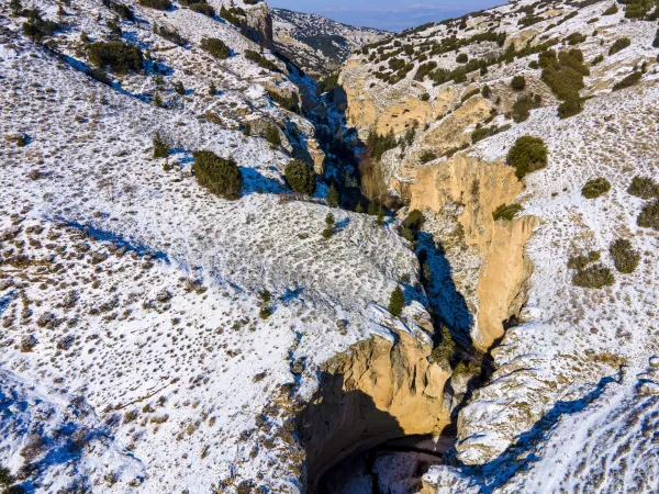 Karla kaplı kanyon manzarası, yeşil ağaçlarla kontrast oluşturuyor.