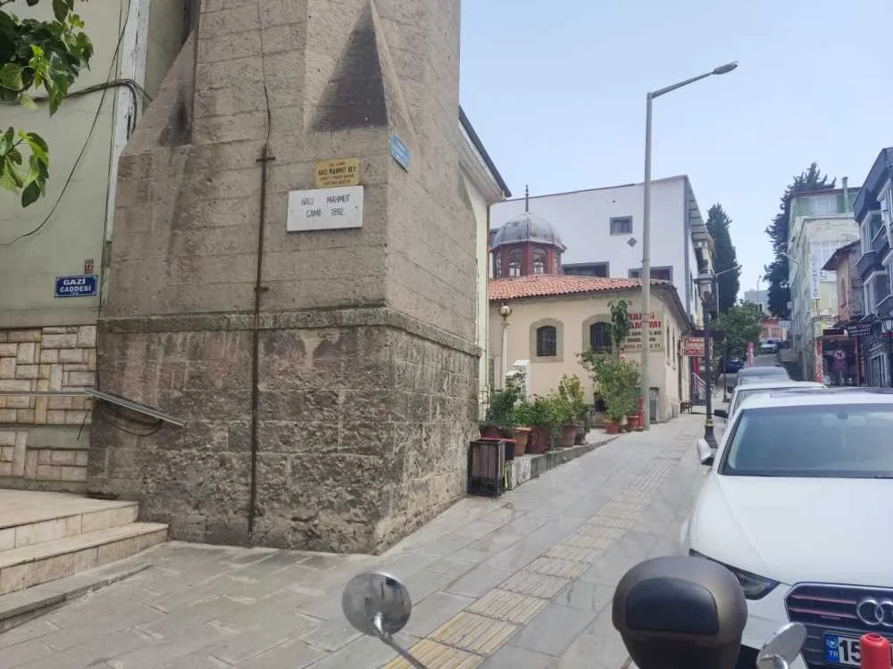 Tarihi Tabak Hamamı - Sakin Sokaklarda Osmanlı Mirası! Dar bir sokakta, taş yapı ve kırmızı çatılı bina ile bitkiler yer alıyor.