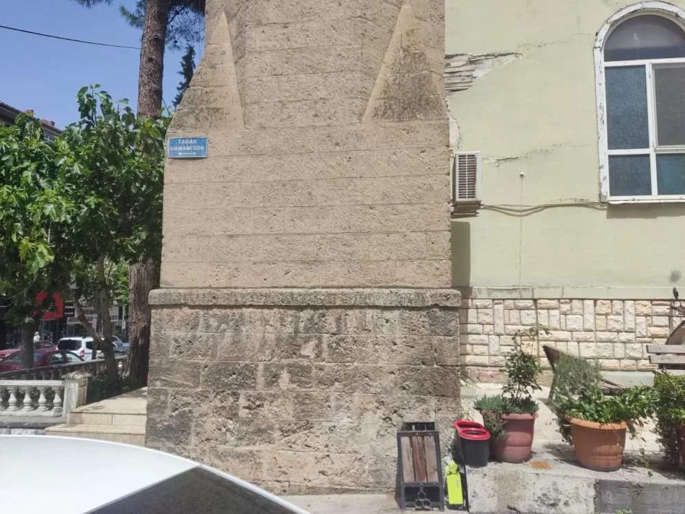 Tarihi Mimari ve Doğal Güzellik - Taş İşçiliği ve Yeşilin Uyumu! Tarihi yapının köşe kısmı, taş işçiliği ve mavi tabela ile çevresinde yeşil ağaçlar.