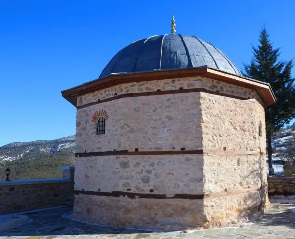 Pembe taşlardan inşa edilmiş Veli Dede Türbesi, metal kubbe ve çevresindeki karla kaplı dağlar ile görülüyor.