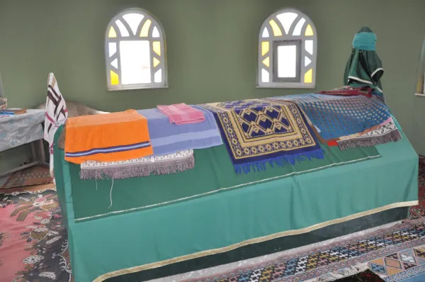 Yeşil odada farklı renklerde örtülerle kaplı bir mezar ve yuvarlak pencereler