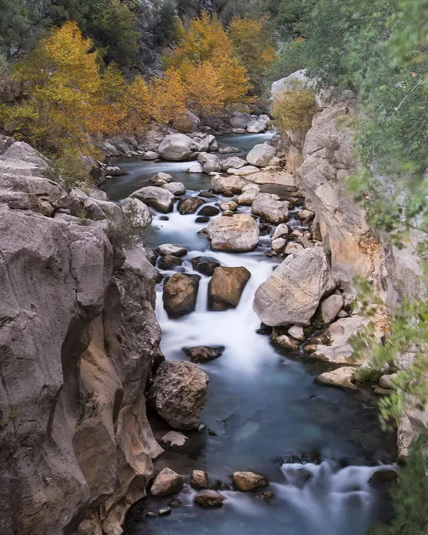 Sonbahar renkleriyle dolu vadi, mavi akarsu ve taşlar huzur veriyor.