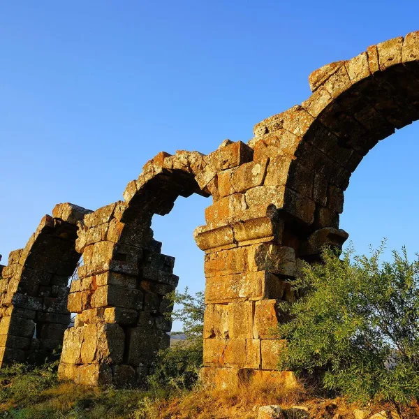 Eski taş kemerler, doğal bitki örtüsü ve açık mavi gökyüzü ile çevrili