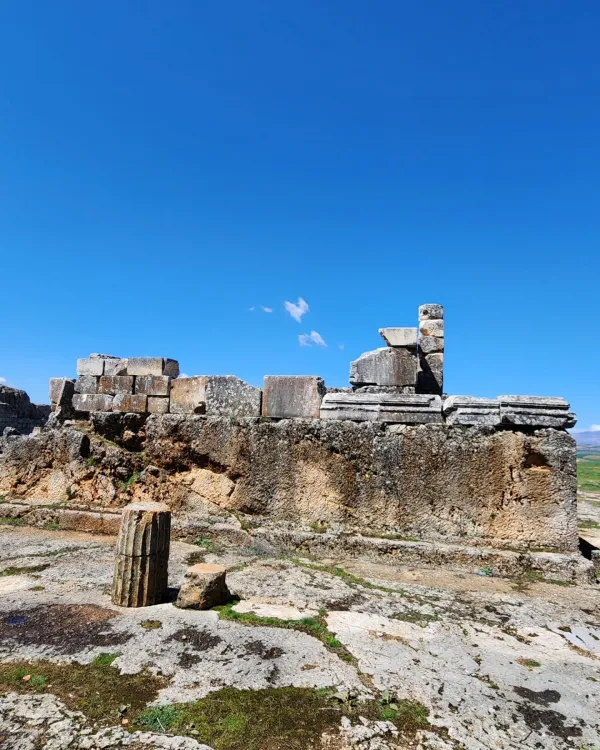 Açık mavi gökyüzü altında antik yapının kalıntıları ve taş duvarlar