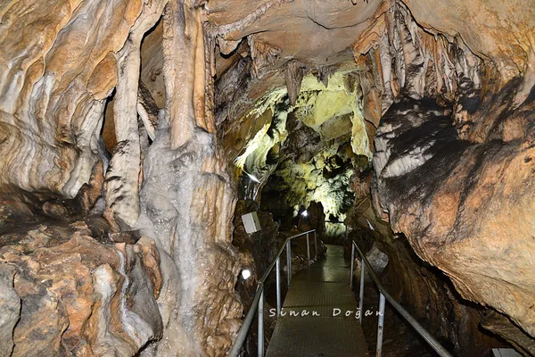 Mağara içindeki çeşitli şekil ve renklerde taş oluşumları, metal yürüyüş yolu ve yapay aydınlatmalar.