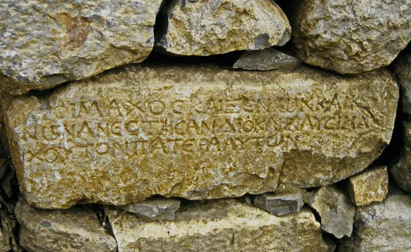 Taş duvar üzerindeki aşınmış eski yazıtlar, tarihsel bir metin içerebilir.