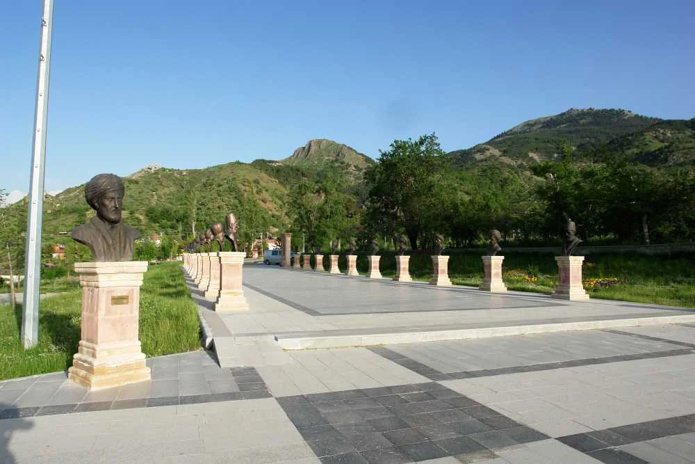 Yeşil ağaçlar ve dağ manzarası eşliğinde heykellerin yer aldığı huzurlu bir park