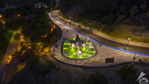 Yeşil aydınlatmalarla süslenmiş meydanda savaş uçağı heykeli ve su havuzları