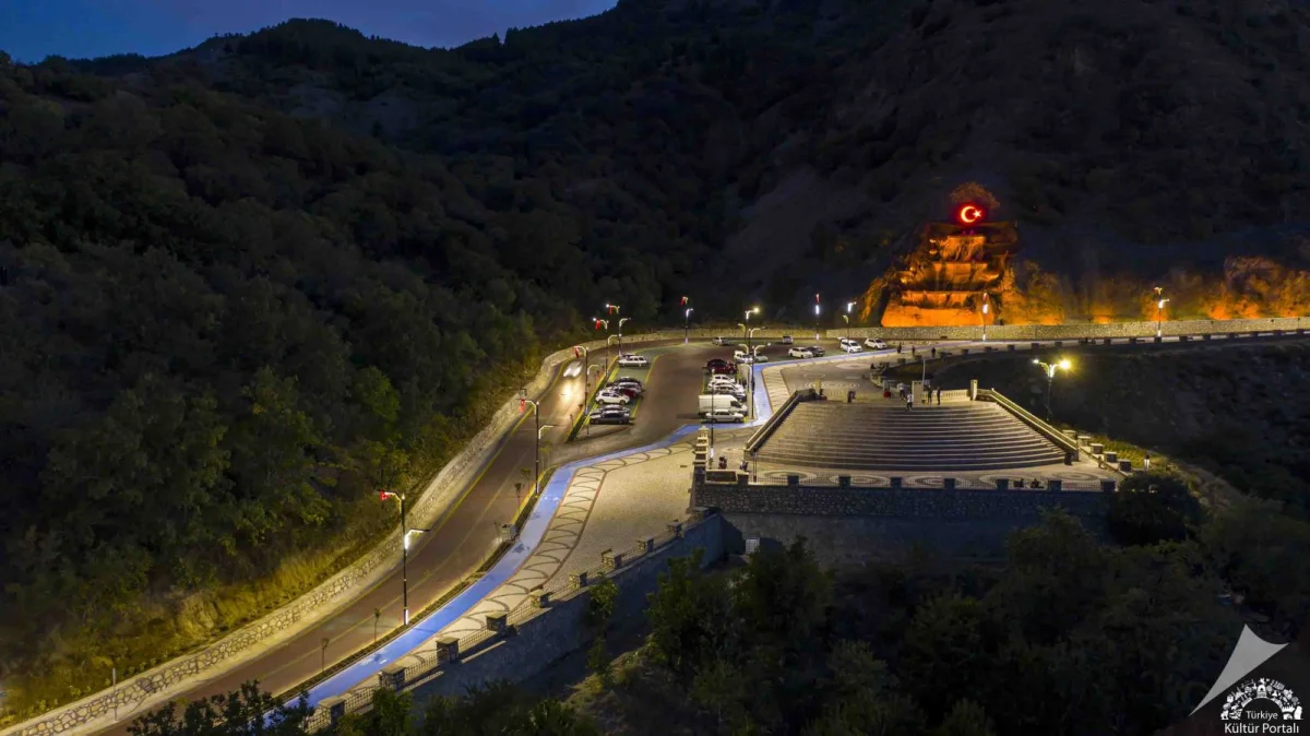 Aydınlatılmış Türk bayrağı ile gece manzarası, geniş park alanı ve merdivenler.