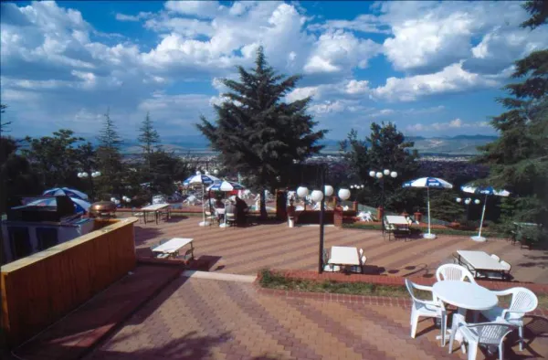 Gökçay mesireliğinde beyaz ve mavi şemsiyelerle örtülü açık hava terası, çam ağaçları ve dağ manzarasıyla çe