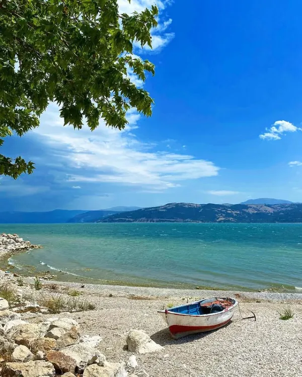 Küçük bir bot, dalgalanan su ve dağlık alanla göl manzarası