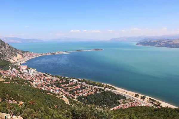 Eğirdir Gölü'nde yemyeşil dağlar ve plaj manzarası.