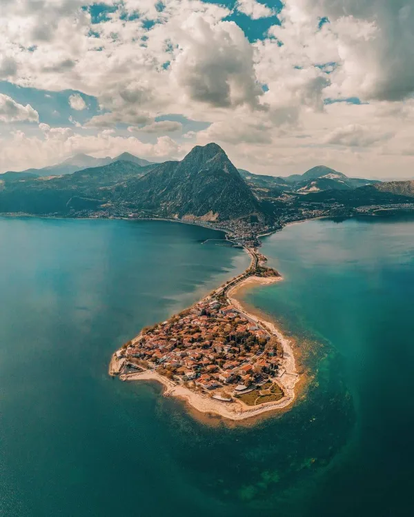 Mavi suyla çevrili yarımada ve küçük evler, arka planda yüksek dağlar.