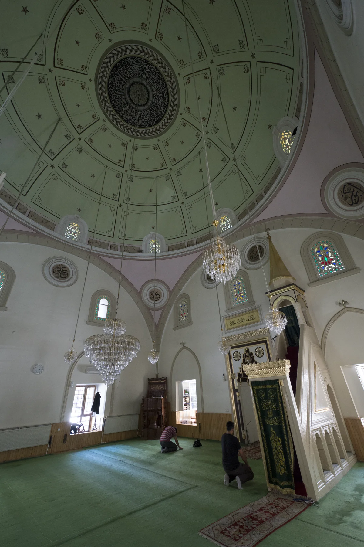 Zarif iç mimarisi, vitray pencereleri ve dua eden kişilerle huzurlu bir cami atmosferi.