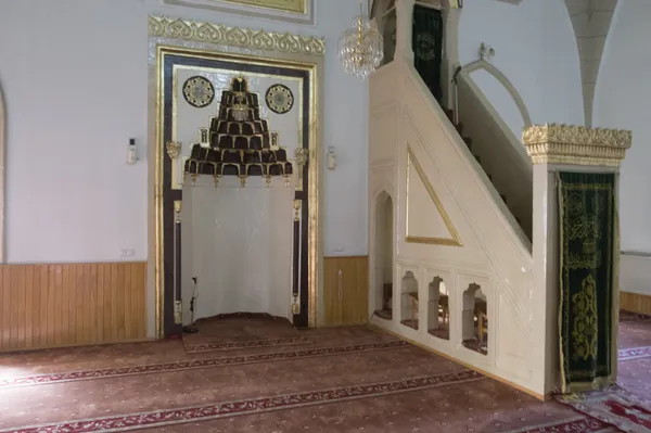 Açık renk duvarlar ve desenli halı ile süslenmiş cami iç mekan görünümü.