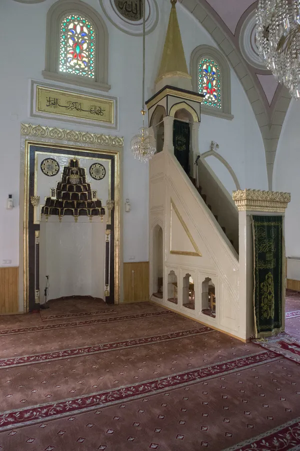 Firdevs Bey Camii'nin mihrap ve minber bölümü, süslemelerle dolu yüksek tavan ve vitray pencereler.