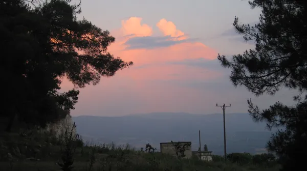 Pastel tonlarında bulutlar ile dolu gökyüzü ve huzurlu doğa manzarası.