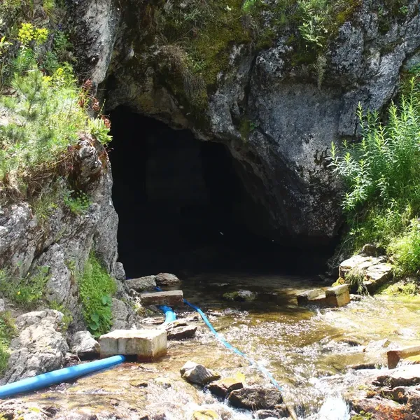 Kaya yarığında karanlık bir mağara girişi ve önündeki akan dere.