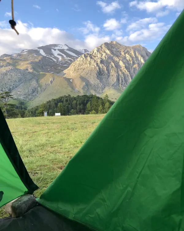 Yeşil çadırdan görünen sarp dağ manzarası ve çimen alanı