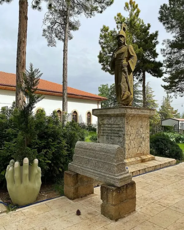 Ertokuş Medresesi'nde altın rengi heykel, beyaz bina ve yeşil bitkilerle çevrili