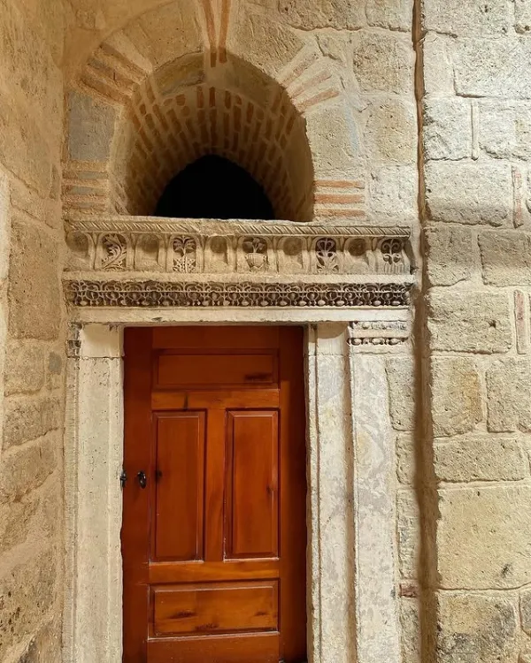 Antik taş duvarlarla çevrili, ahşap kapı ve taş süslemeler.