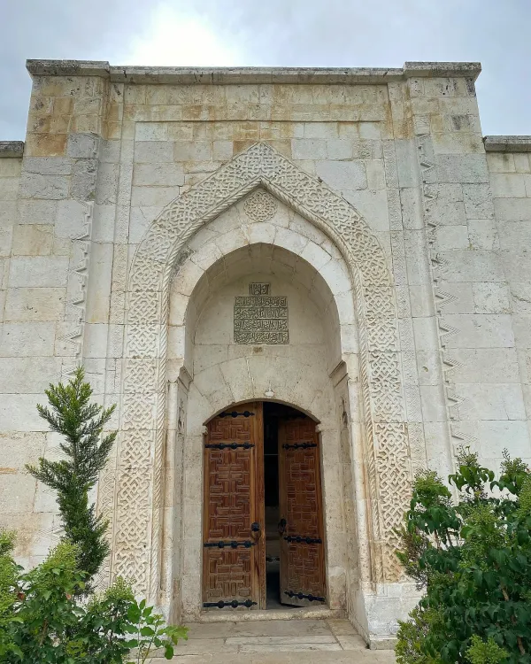Taş işçiliği detaylı büyük kapı, simetrik bitkiler ve açık ahşap kapılarla tarihi bir yapı.