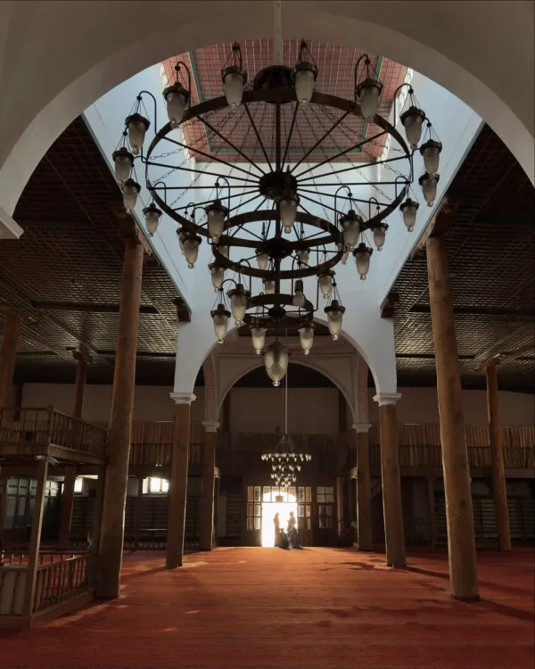 Geniş iç mekânda yüksek duvarlar, avizeler ve kırmızı halı ile geleneksel mimari detaylar