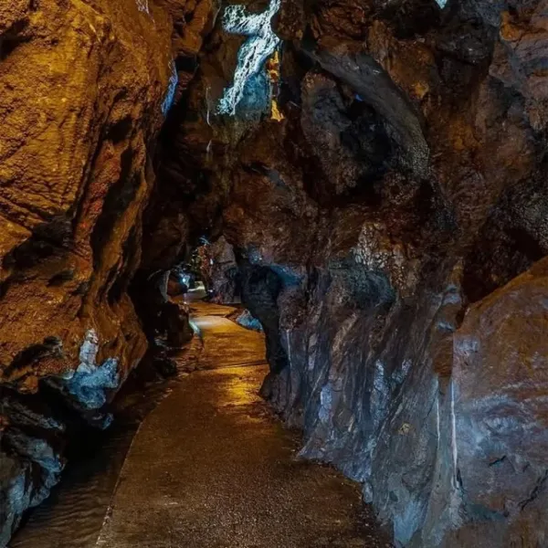 Dar ve kıvrımlı mağara yolu, doğal taşlar ve ışık yansımalarıyla çevrili.