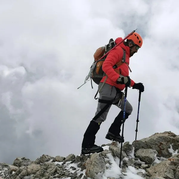 Turuncu montlu dağcı, kayalık zirvede yürürken kar ayakkabılarıyla zorlu bir doğa koşulunda